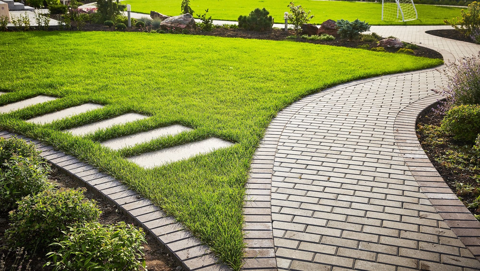 Trädgårdsyta med gräs och stengångar, gröna buskar